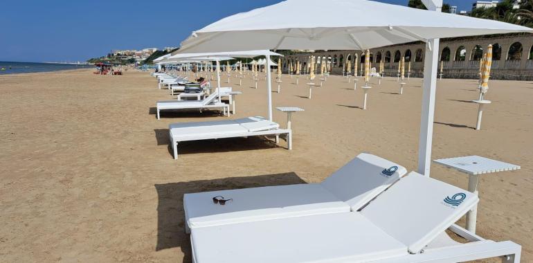 Spiaggia sabbiosa con lettini bianchi e ombrelloni, vista mare.