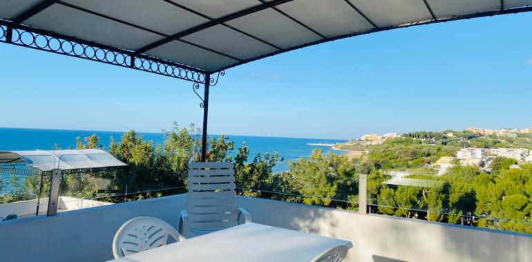 Terrazza con vista mare e colline, cielo sereno.